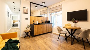A modern hotel room with a wooden floor, a kitchen area with a wooden counter, a dining table with chairs, a large mirror, and a flat-screen TV mounted on the wall. - Estrella 7 Elegancki Apartament W Sercu Torunia (Torun)