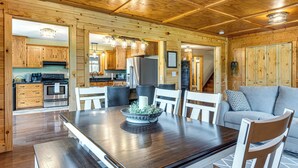 A wooden interior with a dining table, chairs, a sofa, and a kitchen area with cabinets and appliances. - Family-Friendly Milton Home on 14 Acres w/ Hot Tub (Milton)