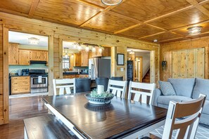 Un interior de madera con una mesa de comedor, sillas, un sofá y una zona de cocina con armarios y electrodomésticos.