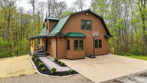 A log cabin with a green roof, a porch, and a driveway. - Family-Friendly Milton Home on 14 Acres w/ Hot Tub (Milton)