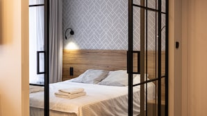 En pænt redt seng med et trægavl, en vægmonteret lampe og en væg med et geometrisk mønster.