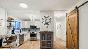 A modern kitchen with white cabinetry, a wooden dining table, and a sliding barn-style door.