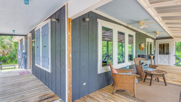 Une véranda couverte avec une terrasse en bois, des meubles en osier et un ventilateur de plafond.