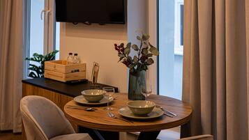 A dining area with a round wooden table, two chairs, a vase with flowers, and a television mounted on the wall.