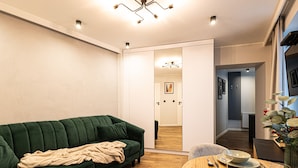 A modern living room with a green sofa, wooden dining table, and a mirror reflecting the hallway. - Estrella 4 Ekskluzywny Pobyt Blisko Restauracji i Kawiarni (Torun)