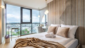 A modern hotel room with a large bed, a view of the city, and a desk with a chair. - Rio 1 Studio z Niezapomnianym Widokiem na Bydgoszcz (Bydgoszcz)