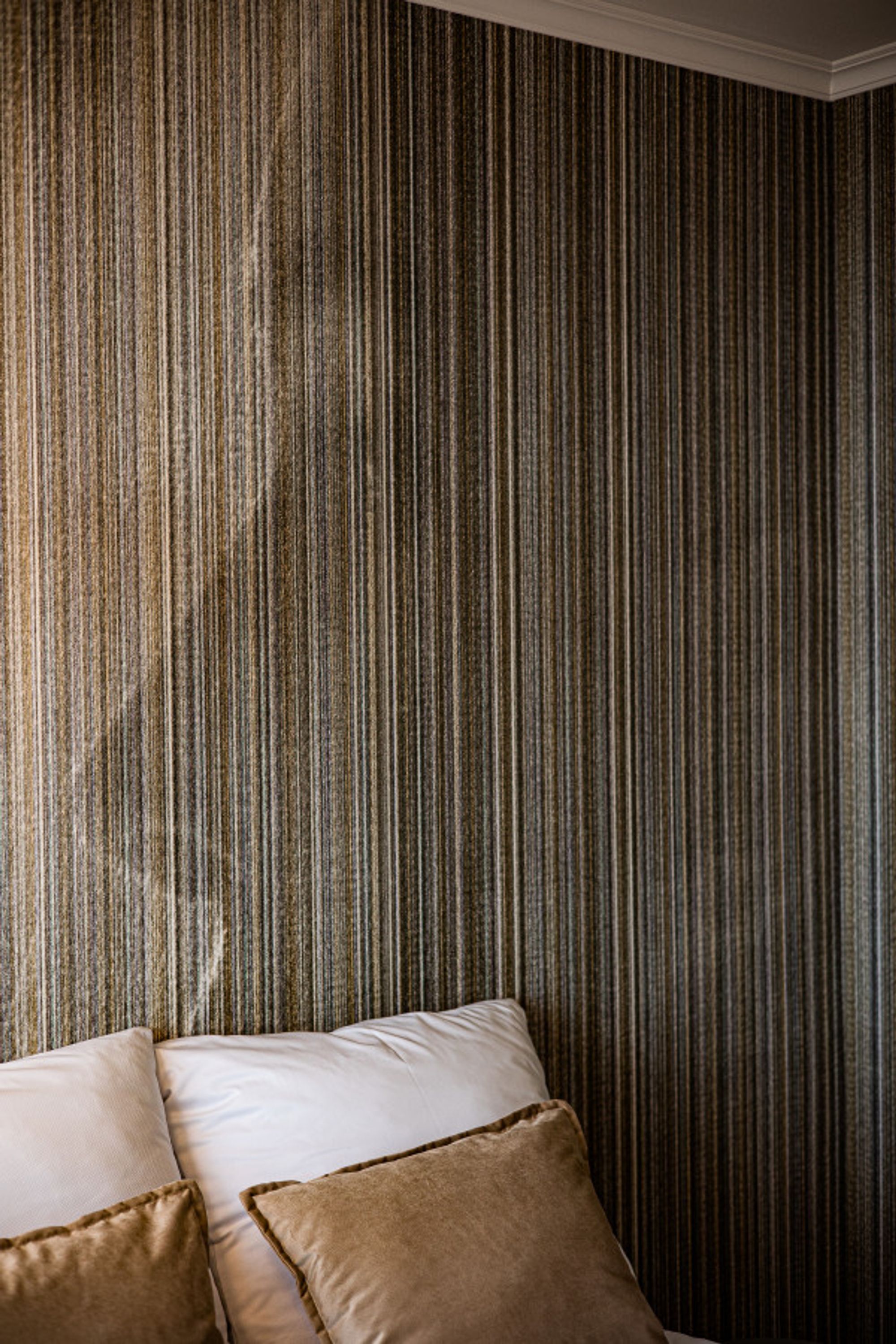 A room with a striped wallpaper and a bed with white and brown pillows.