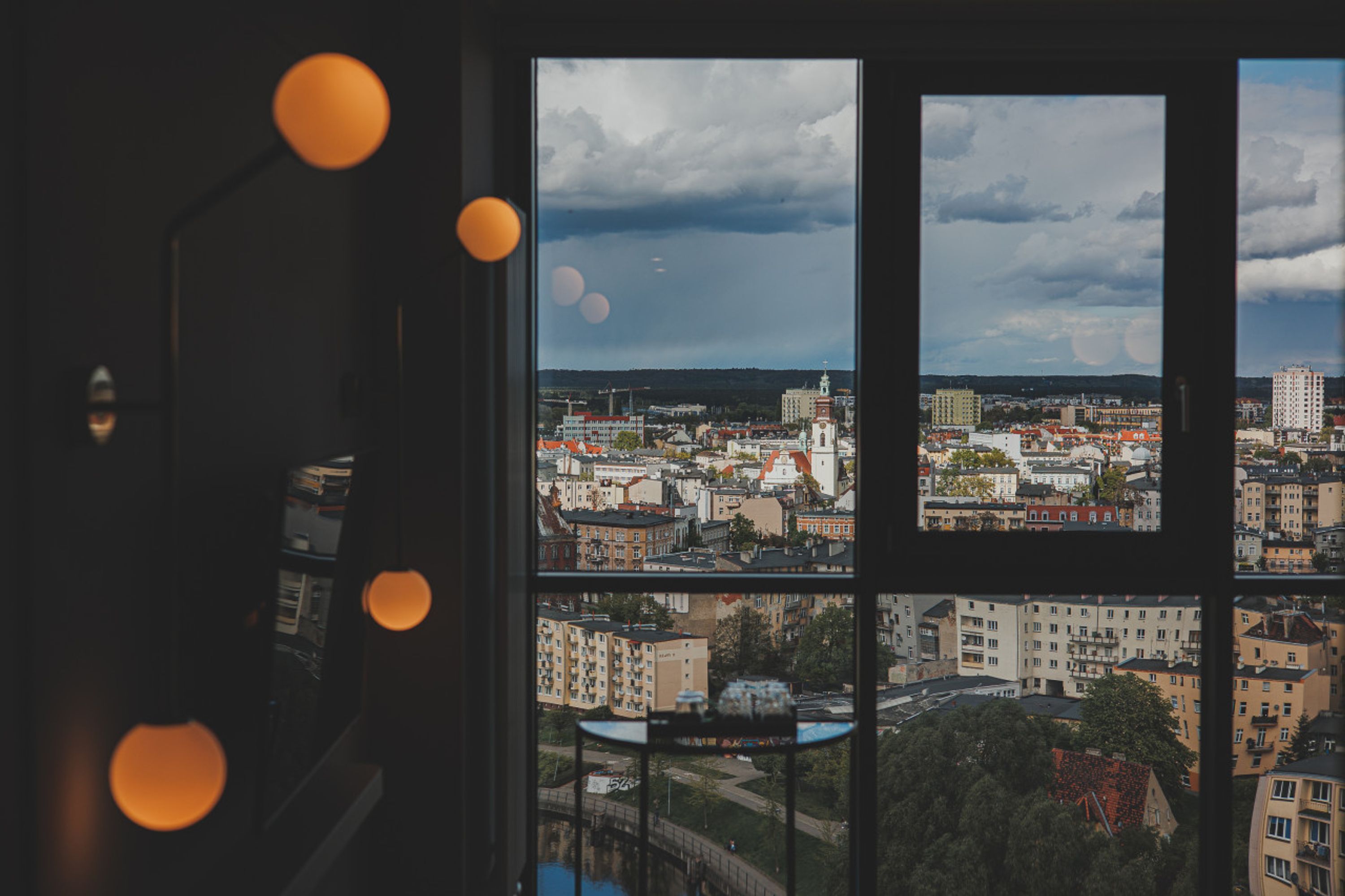 A view through a window with a cityscape, including buildings and a church, with a cloudy sky.