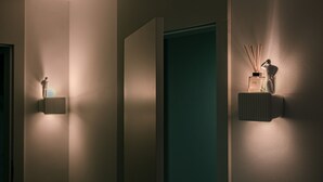 Een hal met een blauwgroene deur, een wandlamp en een kleine tafel met een fles en rietverspreider.