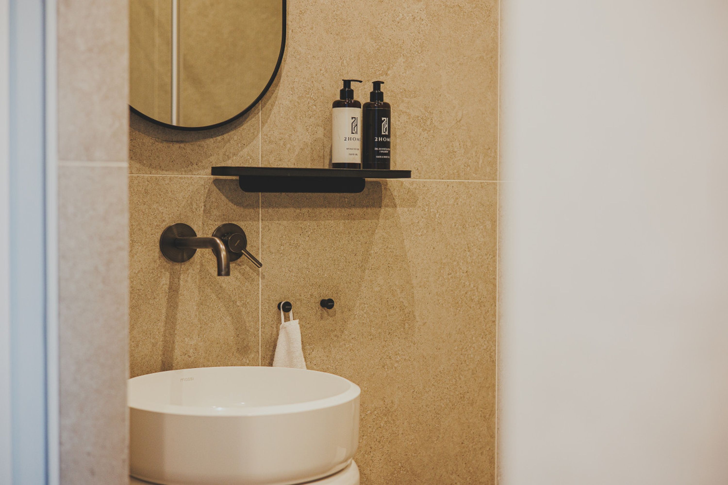 A bathroom with a white sink, a towel hanging on a rack, and two bottles on a shelf above the sink.