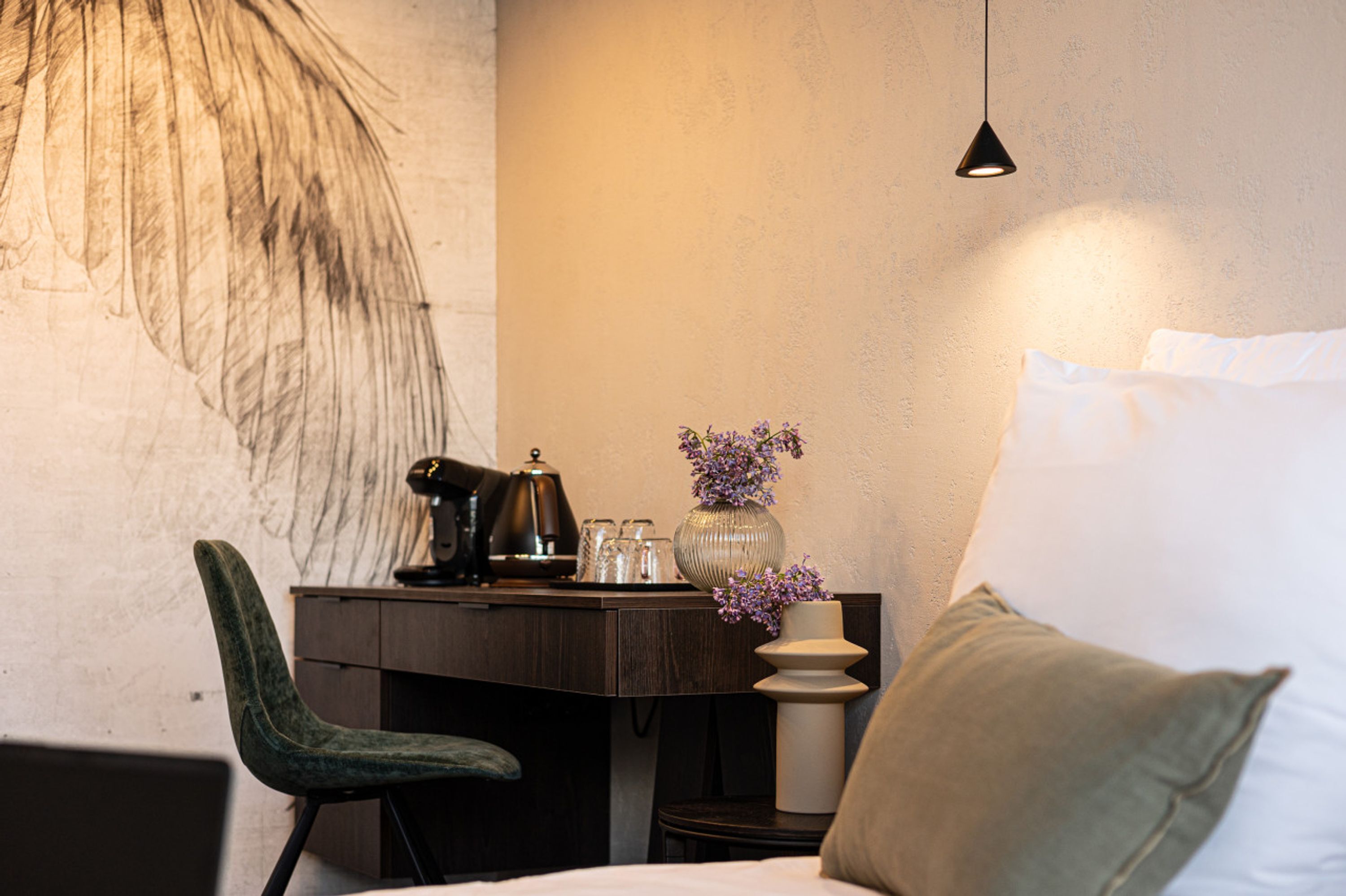 Une pièce comprenant un lit, un bureau avec une lampe, une chaise et un vase avec des fleurs.