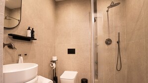 Een moderne badkamer met een wit wastafelmeubel, toilet en douche. Er zijn planken met toiletartikelen en een spiegel boven het wastafelmeubel.