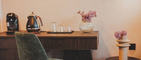 A wooden desk with a coffee maker, a kettle, and a vase with flowers.