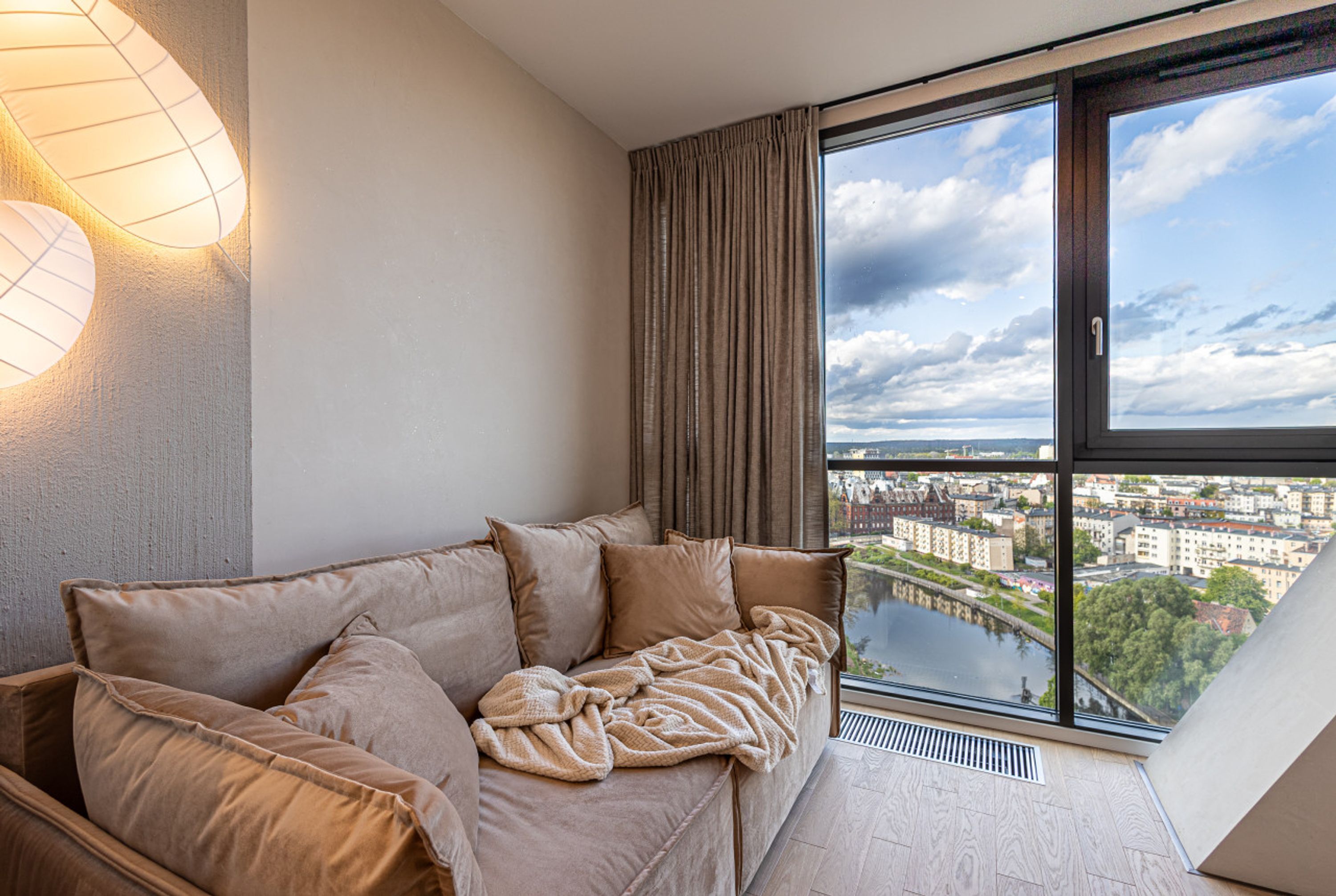 Ein modernes Wohnzimmer mit großem Fenster, einer Couch und einer Wandleuchte.