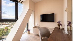 A modern living room with a large window, a flat-screen TV mounted on the wall, a dining table with chairs, and a small side table with decorative items. - Rio 2 Panorama Bydgoszczy Luksus w Centrum (Bydgoszcz)