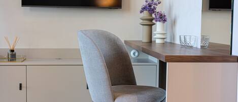 A modern living room with a grey upholstered chair, a wooden coffee table, and a flat-screen TV mounted on the wall.