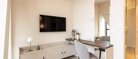 Ett modernt vardagsrum med en platt-TV som är monterad på väggen, ett matbord med stolar och en stor spegel som reflekterar rummet.