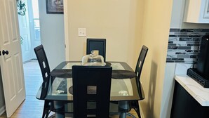 Zona pranzo con tavolo in vetro, sedie nere e macchina da caffè nera.