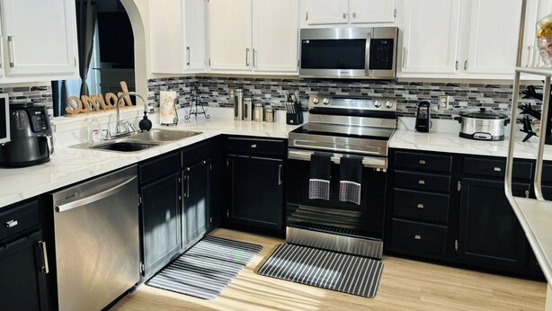 Una cucina moderna con mobili bianchi, elettrodomestici in acciaio inossidabile e un piano di lavoro nero.