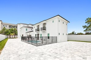 A modern two-story house with a swimming pool, white exterior, and a paved courtyard.