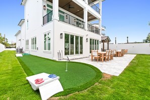 Une maison à deux étages dotée d’un patio comprenant un terrain d’entraînement au golf, un ensemble de mobilier de jardin et une table de billard.