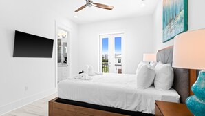 Ein modernes Schlafzimmer mit einem Bett, einem Deckenventilator, einem Fernseher und einem Fenster mit Blick auf Gebäude.