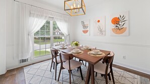 Ein Esszimmer mit Holztisch, gedeckten Plätzen für sechs Personen, weißen Vorhängen und zwei Wandbildern.