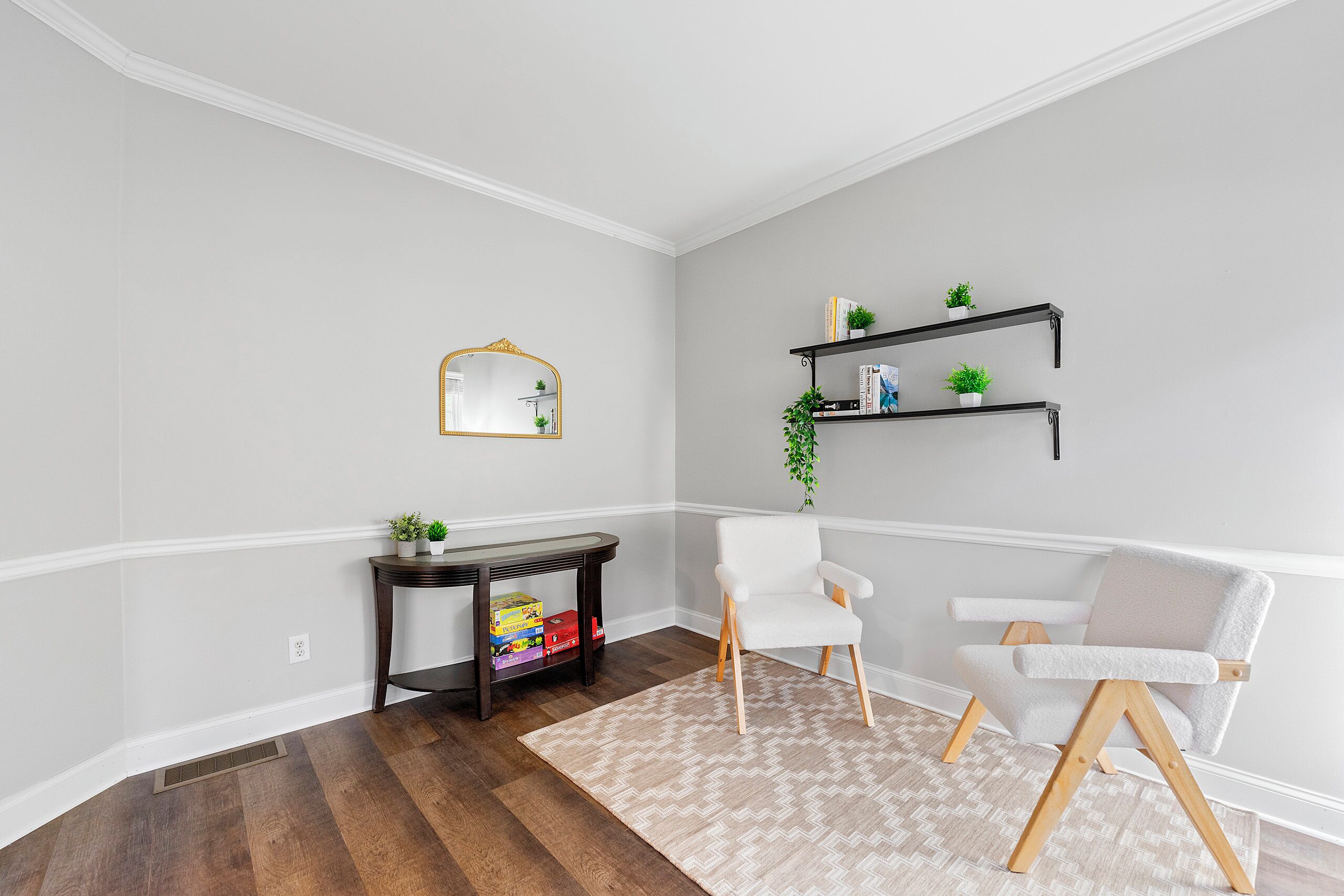 A room with a white chair, a small table with a mirror, and a shelf with plants.