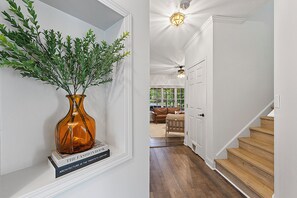 A hallway with a wooden staircase, white walls, and a door leading to a living area with a brown leather sofa.