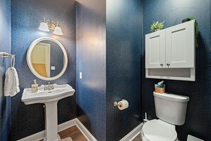 A bathroom with a white pedestal sink, a round mirror, a toilet, and a cabinet above the toilet. - 🌟 MODERN 5-BEDROOM🛏️, PERFECT FOR LARGE FAMILIES! SPACIOUS SUNROOM ☀️ (Lawrenceville)