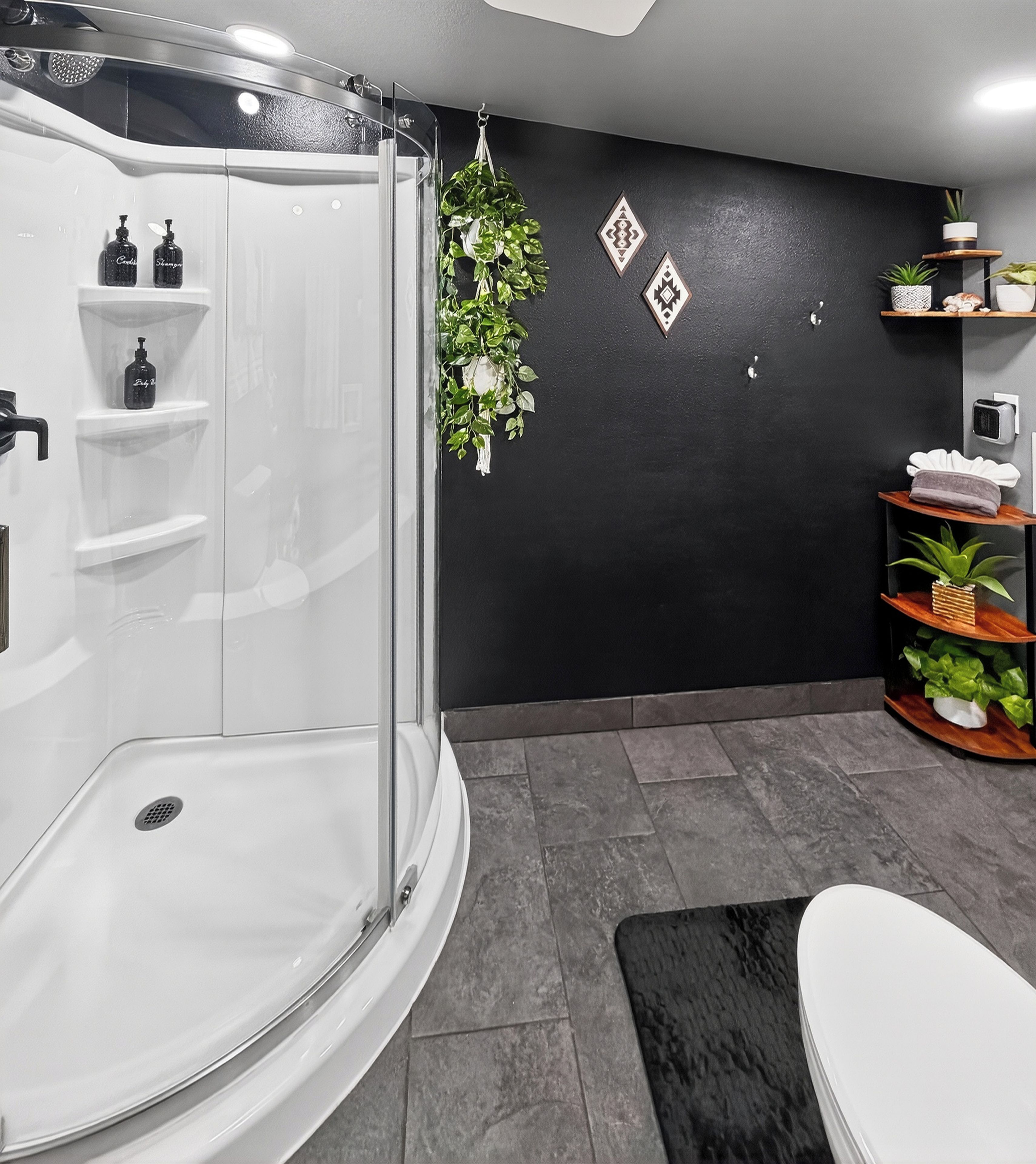 Un baño moderno con ducha envuelta en vidrio, inodoro blanco y pared negra con detalles decorativos.