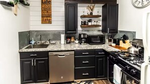 A modern kitchen with black cabinets, a stainless steel dishwasher, a microwave, and a stove. There is a wall clock and a sign with motivational words.