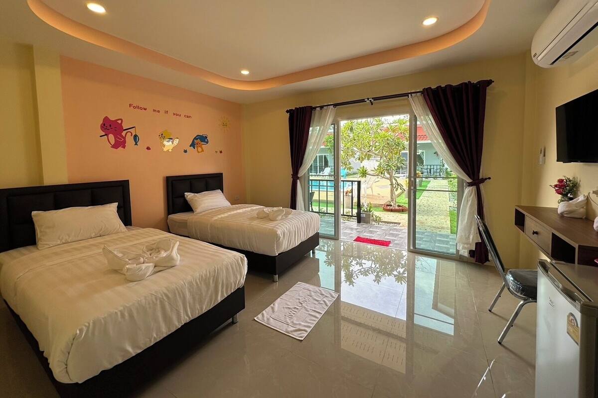 Quarto de hotel com duas camas, uma escrivaninha, televisão e vista para a área externa.