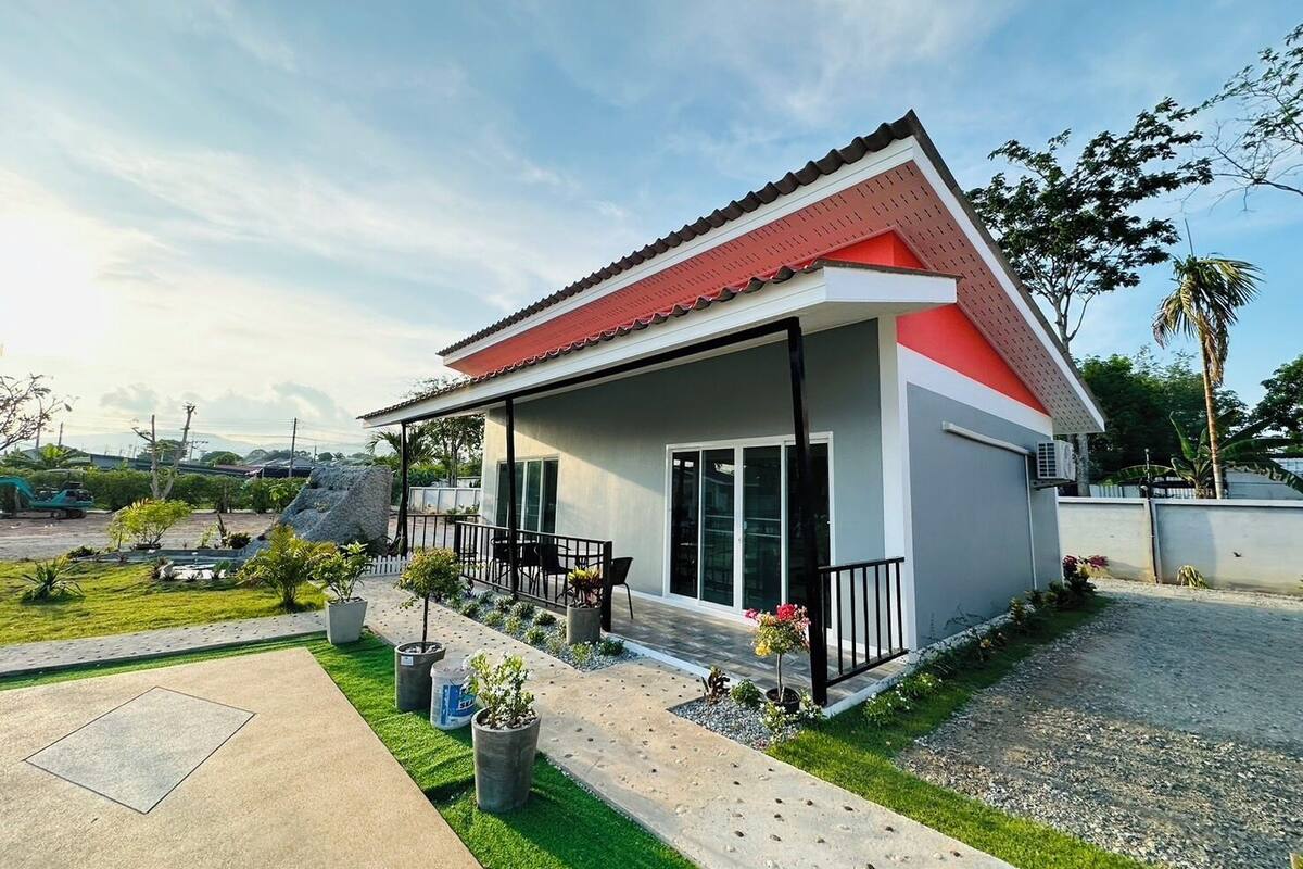Uma casa moderna de dois andares com telhado vermelho, varanda coberta e um jardim bem cuidado.