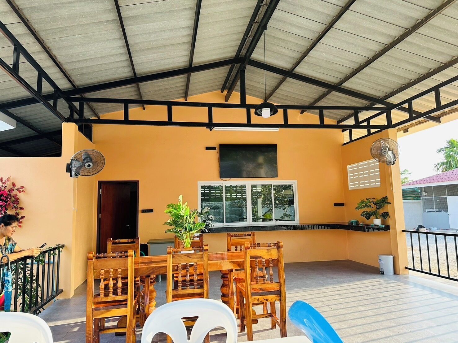 Eine Terrasse im Freien mit einem Holztisch und -stühlen, einem Blumentopf und einem an der Wand befestigten Fernseher.