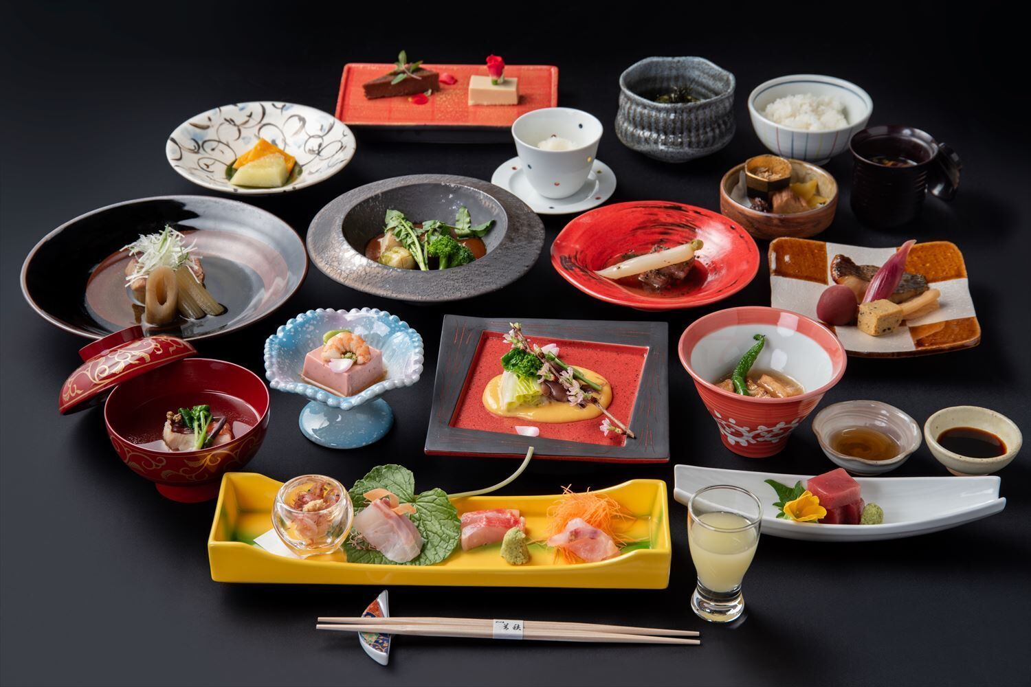 A variety of dishes and bowls of food, including sushi, sashimi, and other Japanese cuisine, arranged on a table.
