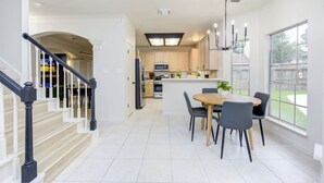 Een moderne keuken met een centraal eiland, een eethoek met een tafel en stoelen, en een trap naar een ander niveau.