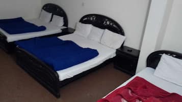 Two single beds with black frames and white bedding, a small bedside table with a lamp, and a brown carpeted floor.