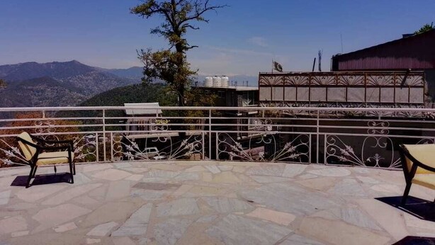 Um terraço com chão de pedra, grades de metal e duas cadeiras.