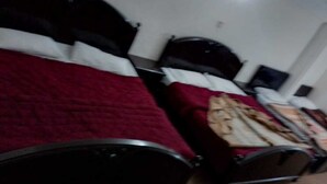 Quarto com duas camas, cada uma com cabeceira e almofadas. Há uma mesinha de cabeceira com luminária e uma cadeira.