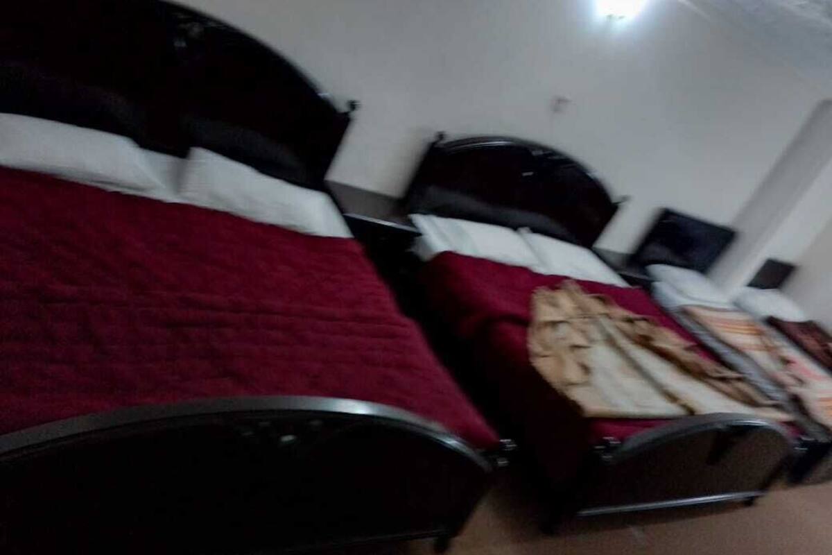 A room with two beds, each with a headboard and pillows. There is a small table with a lamp and a chair.