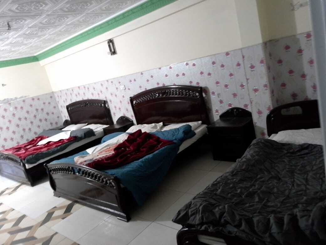 A bedroom with three single beds, a wooden headboard, a tiled floor, and a patterned wall.