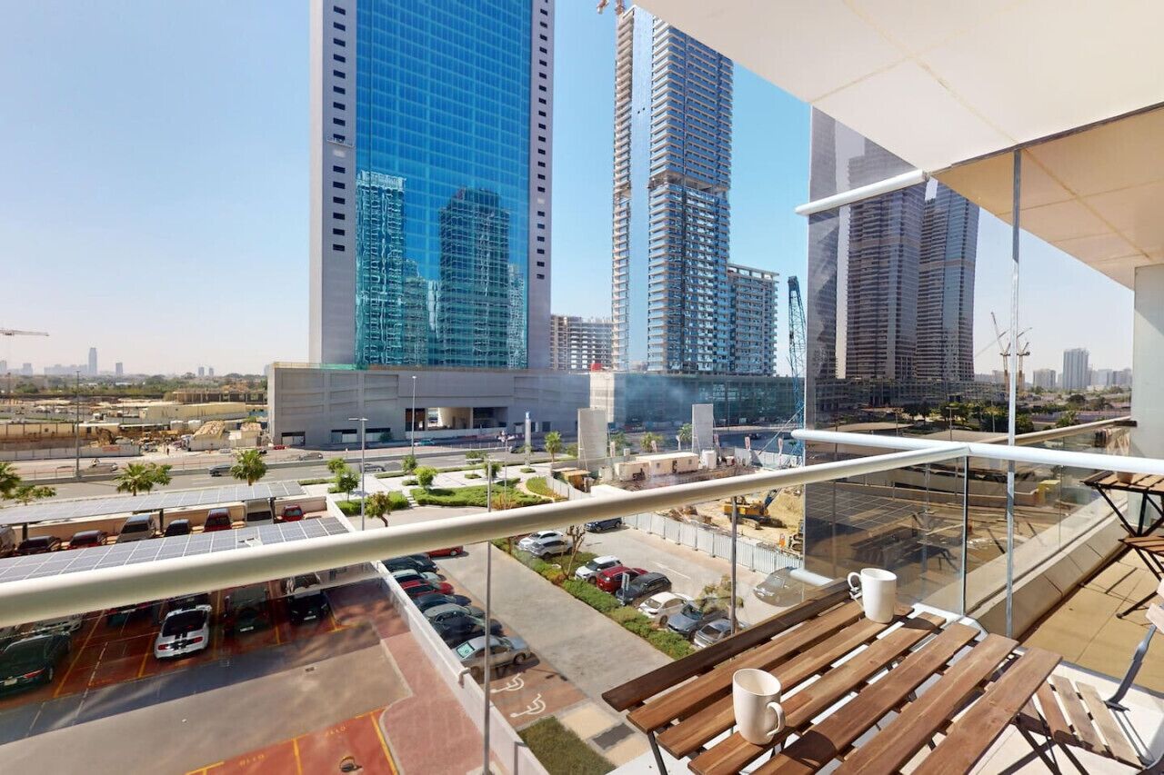 A high-rise building with a modern glass facade, a parking lot below, and a balcony with wooden furniture.
