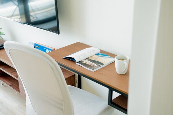 A modern room with a wooden desk, a white chair, a magazine, a white mug, and a flat-screen TV on the wall.