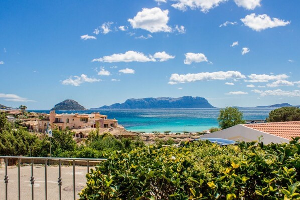 A coastal town with Mediterranean architecture, a clear blue sea, and distant mountains.