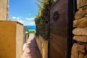 A narrow pathway leading to a wooden gate with a stone wall on one side and a view of the sea on the other.