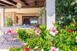 An outdoor patio with stone walls, a table with chairs, and flowering plants.
