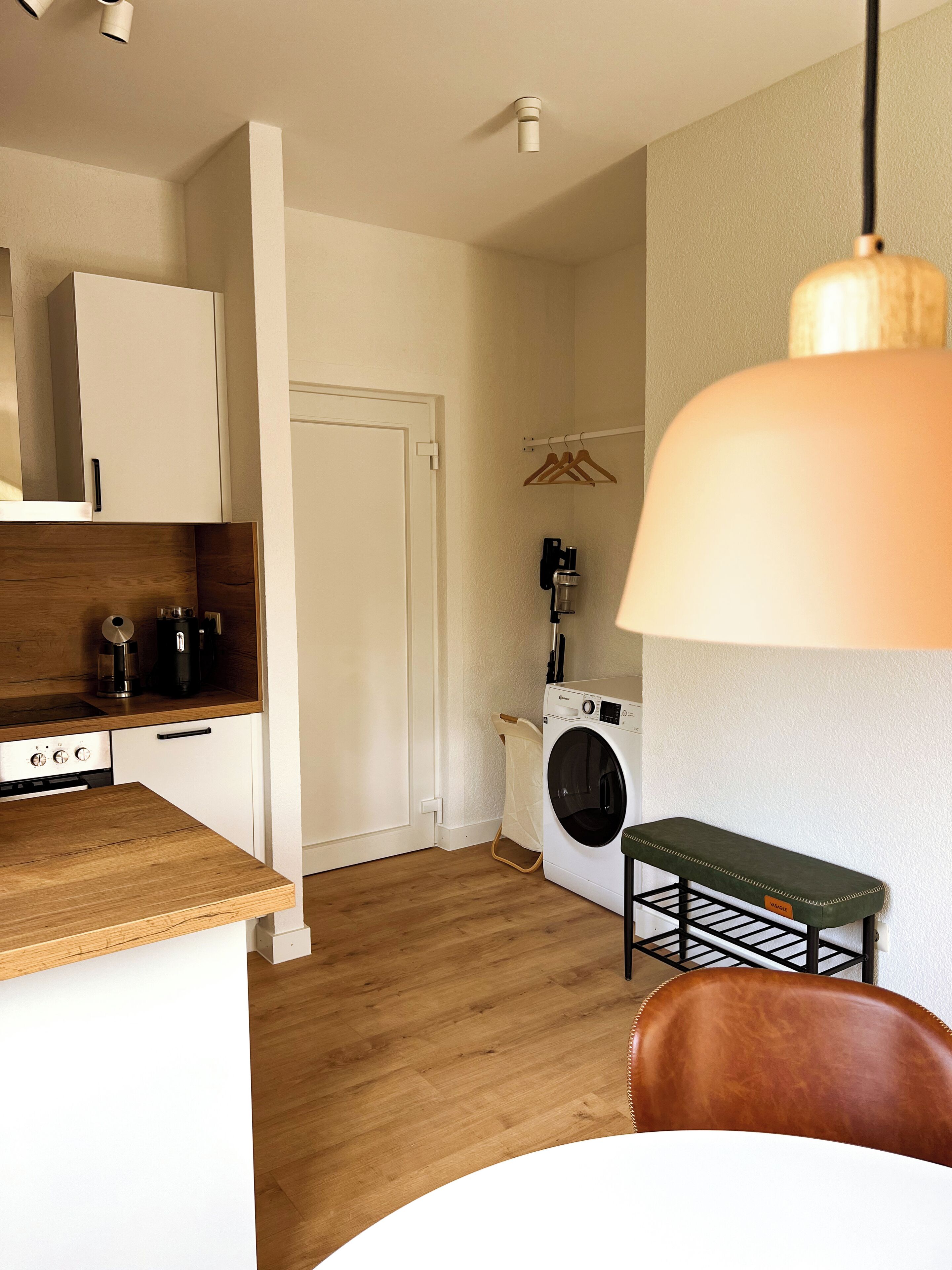 Una cocina compacta con encimera de madera, lavadora y un banco.