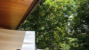 Un balcone con ringhiera in legno, un muro bianco e vista su alberi verdi.