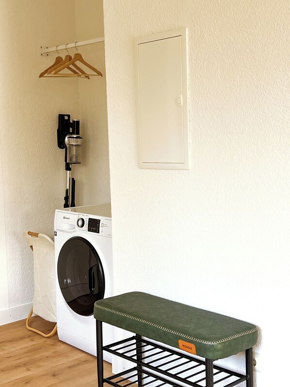 A laundry area with a washing machine, a drying rack, and a bench.